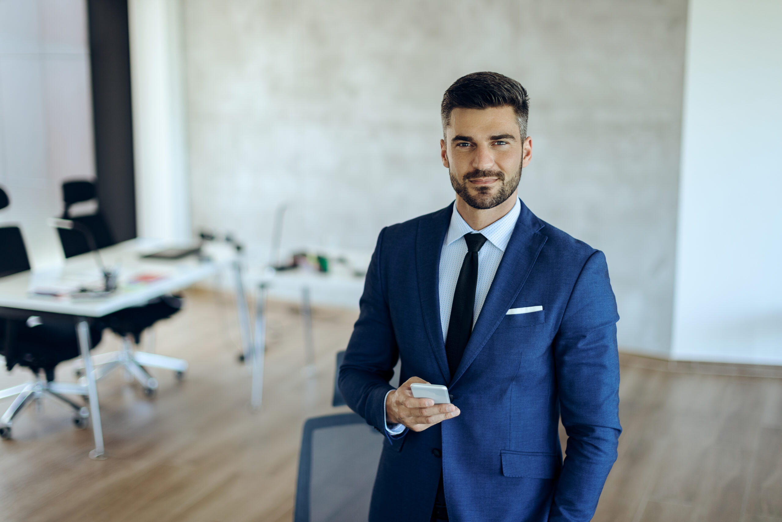 Smiling entrepreneur text messaging on smart phone in the office and looking at camera.